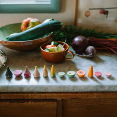 Veggies von Grapat - handbemaltes Holzgemüse liegt auf Arbeitsplatte neben echtem Gemüse