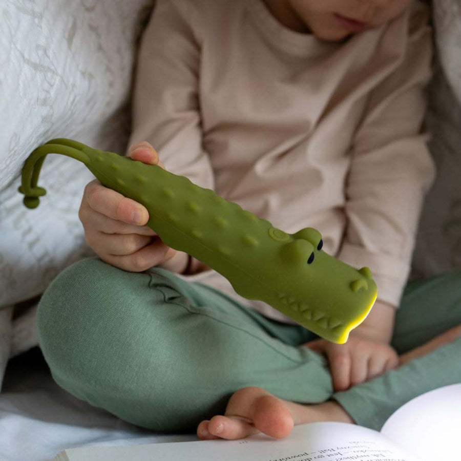 Kind hat Taschenlampe Krokodil von Rabbit & Friends unter der Bettdecke beim Lesen an